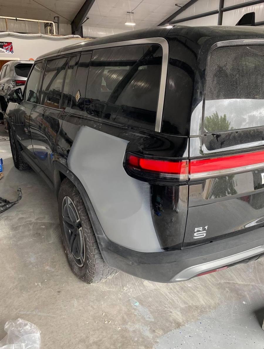 Black Rivian R1S in the shop with the rear quarter panel in gray primer during paint repair